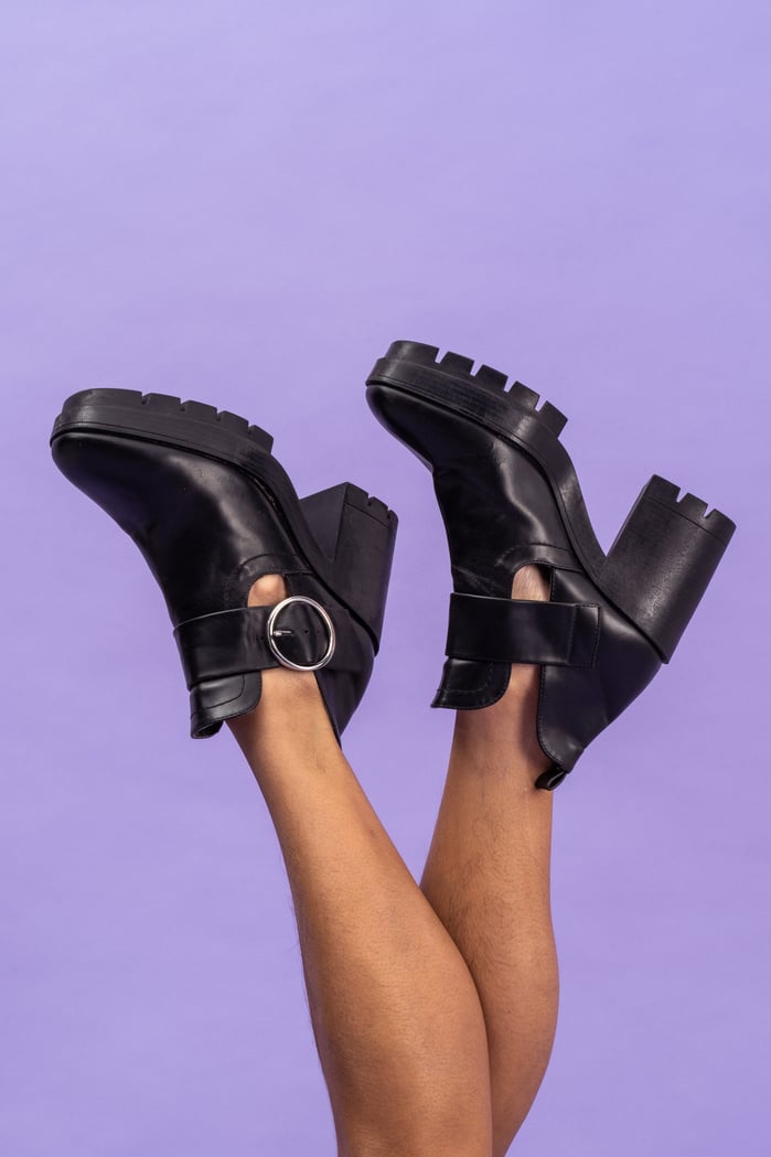 Legs Wearing Black Block Heels on Purple Background